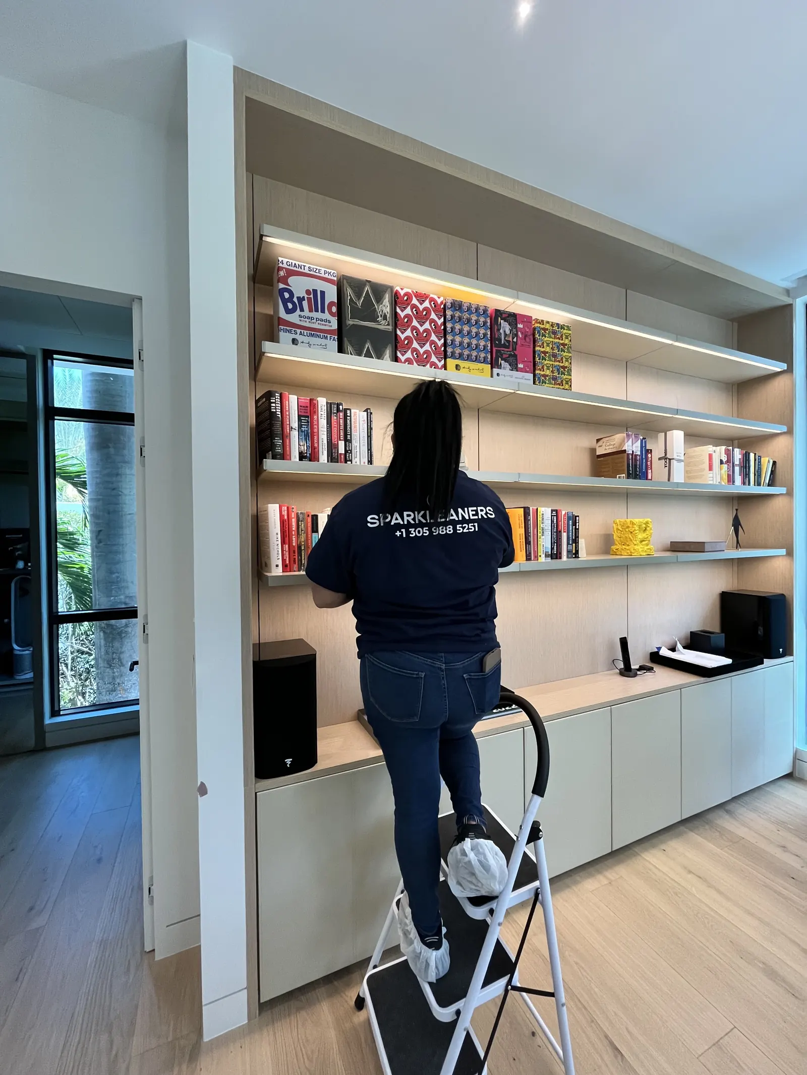 Sparkleaners cleaner dusting the shelves of a modern Miami home